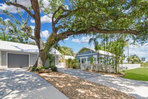A residential property with a garage, a paved driveway, and a white picket fence. - Surfside Oasis ~tropical Pool! Walk to the Beach! (St. Augustine)