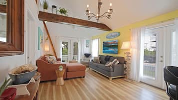 A spacious living room with a wooden floor, a chandelier, and a large window with curtains.