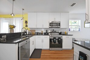 Una cocina moderna con gabinetes blancos, un microondas de acero inoxidable, un horno y un lavavajillas.