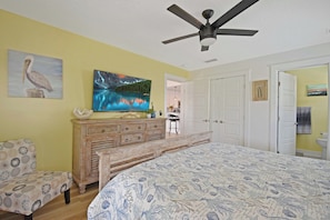 A bedroom with a bed, a dresser, a chair, a ceiling fan, and a painting of a mountain lake. - Surfside Oasis ~tropical Pool! Walk to the Beach! (St. Augustine)