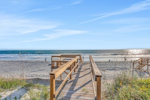 Une promenade en bois qui mène à une plage, avec un ciel dégagé.