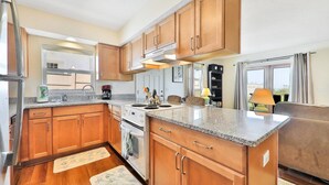 Una cocina moderna con armarios de madera, encimeras de granito, una estufa y una ventana con vistas a un balcón.