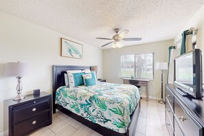 A bedroom with a bed, nightstands, a ceiling fan, a TV, and a window with blinds. - Sun-kissed Beach Condo With Amazing Pool, Tennis & Patio - Steps to the Beach! (St. Augustine)