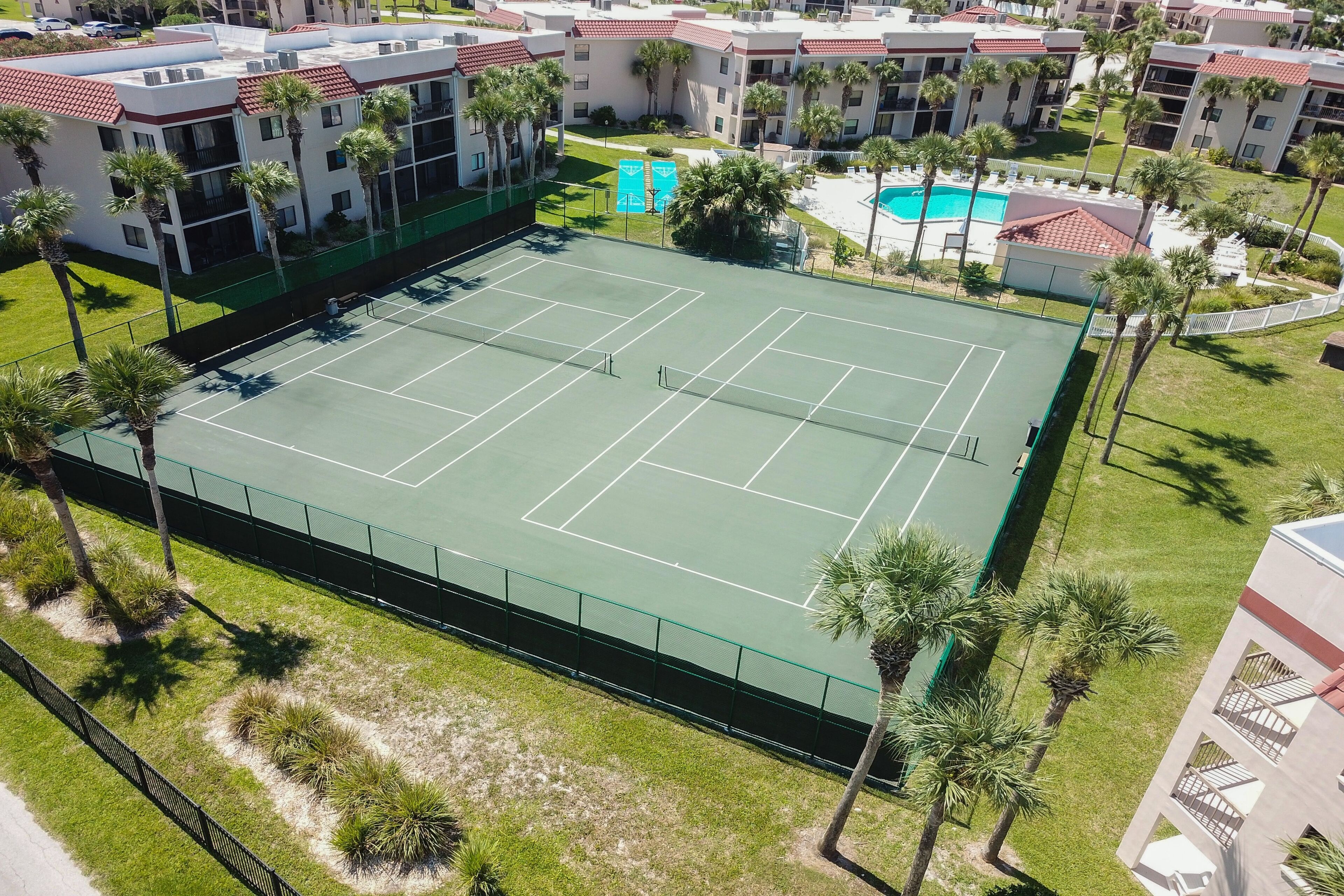 An aerial view of a tennis court surrounded by palm trees and buildings.