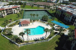An aerial view of a hotel with a swimming pool, tennis courts, and a landscaped area with palm trees. - Sun-kissed Beach Condo With Amazing Pool, Tennis & Patio - Steps to the Beach! (St. Augustine)