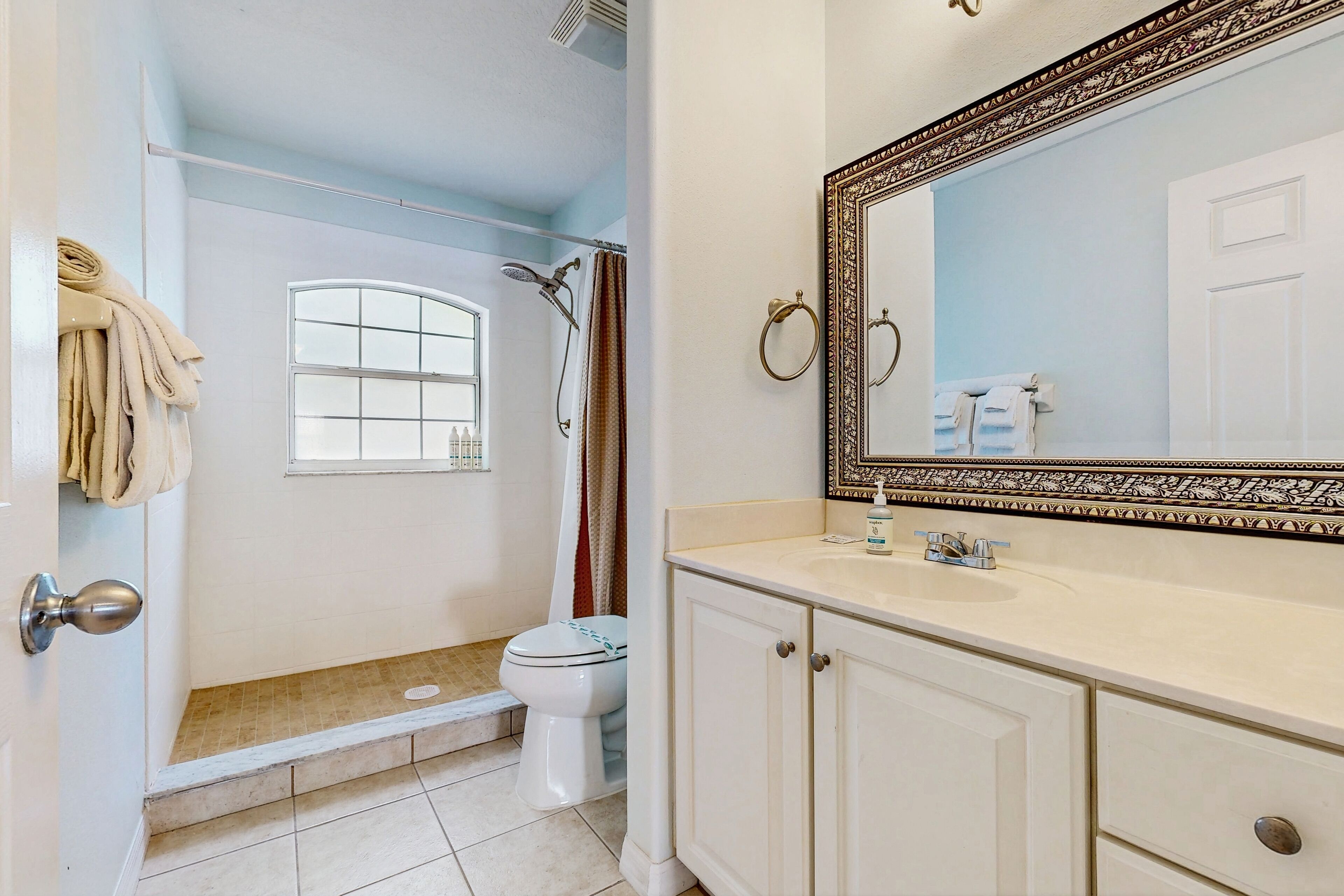 A bathroom with a shower, toilet, vanity, and a large mirror.
