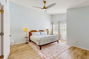 A bedroom with a bed, bedside lamps, a ceiling fan, a window with blinds, and a wooden floor. - Spacious Townhouse With Private Balcony, Waterview, Pool and Wifi (Palm Coast)