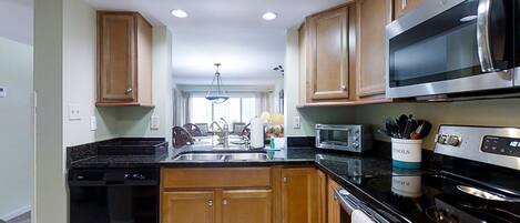 A kitchen with wooden cabinets, a black dishwasher, a stainless steel microwave, and a stove.