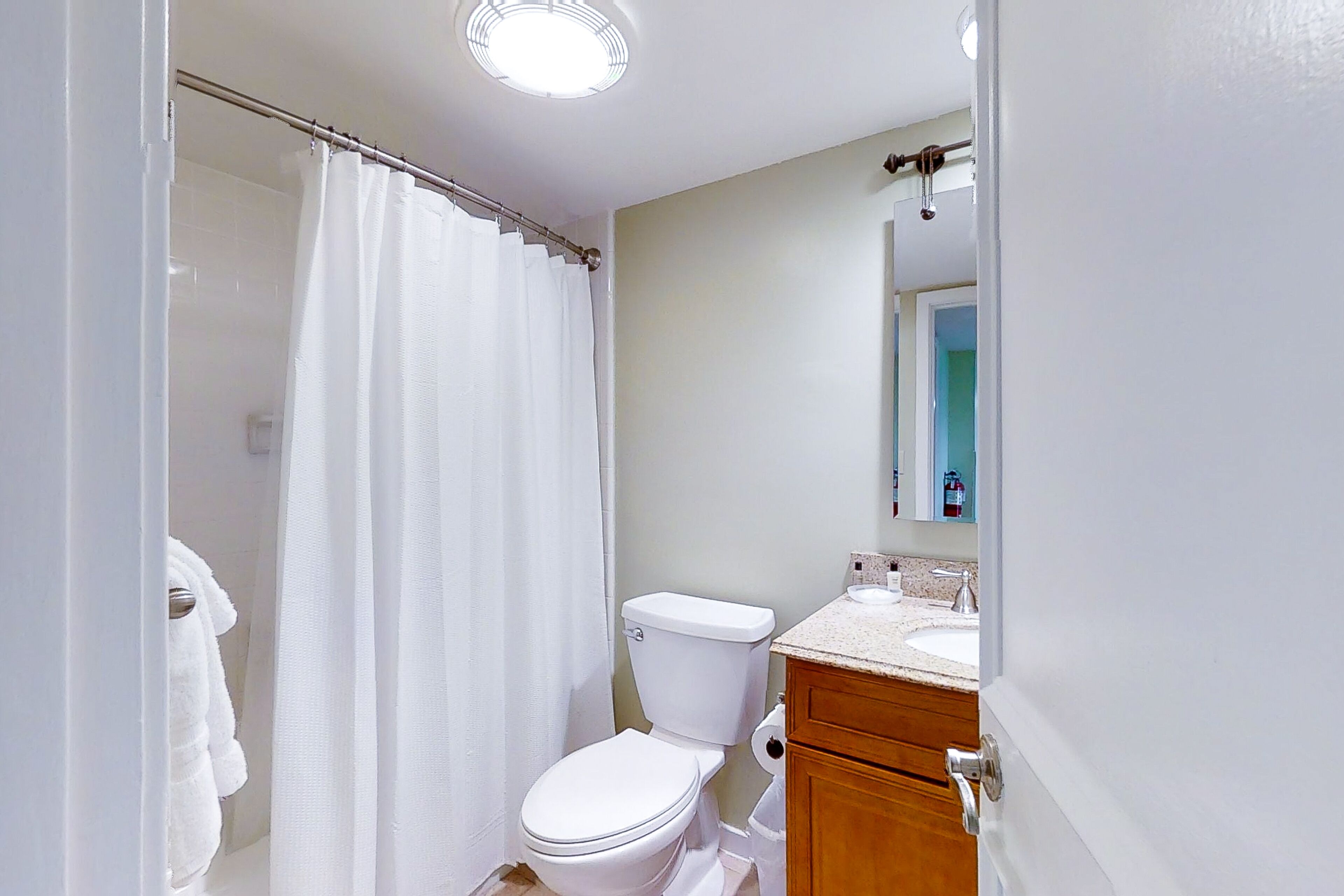 A bathroom with a white toilet, a shower curtain, a sink, and a mirror.