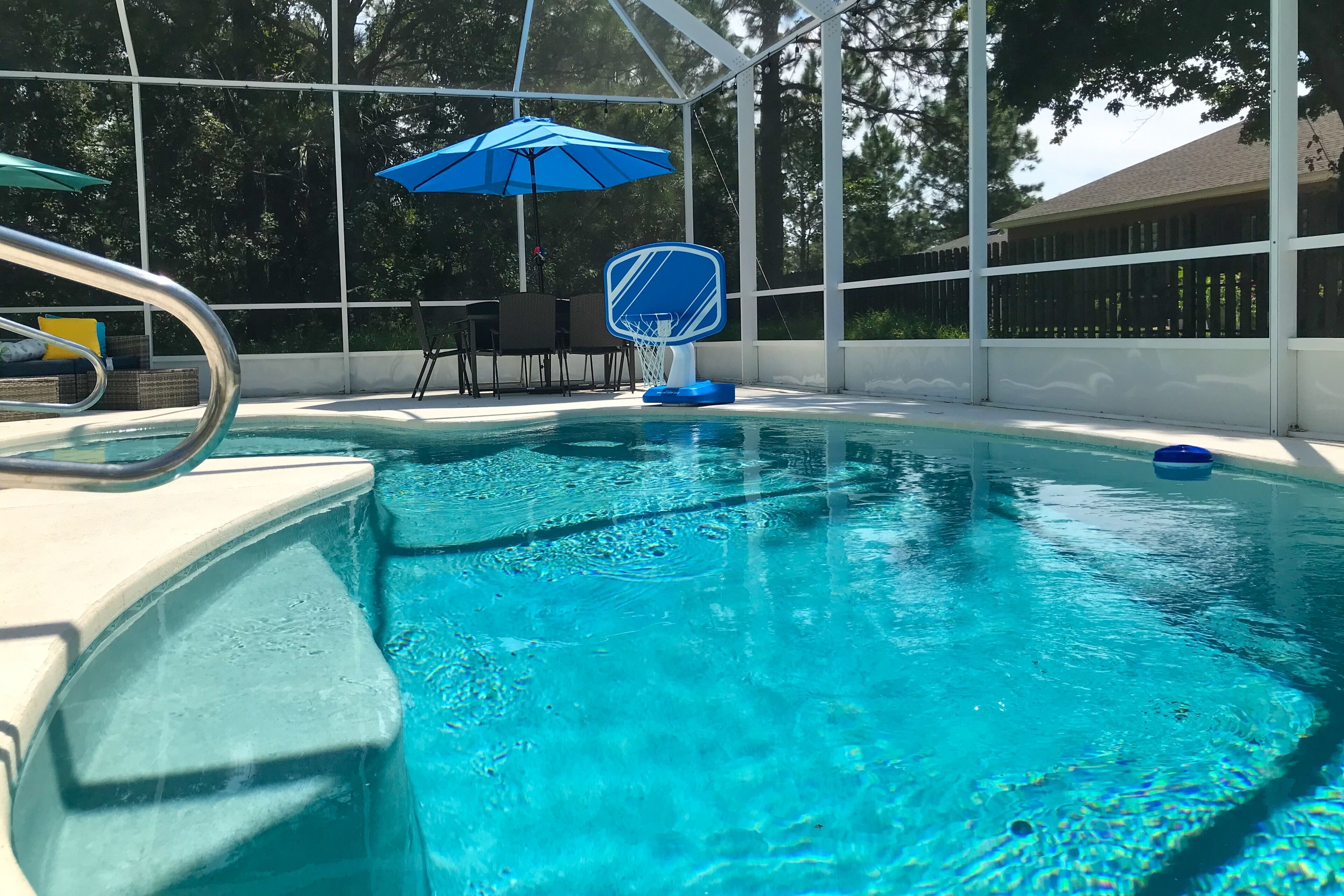 Ein Swimmingpool mit blauem Sonnenschirm, einem Basketballkorb und einer Liege.