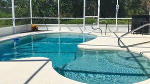 A swimming pool with clear blue water, a white deck, and a metal ladder. - The Barefoot Bungalow House in Palm Coast With an Enclosed Pool & Grill (Palm Coast)