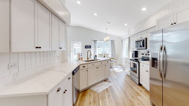 A modern kitchen with white cabinetry, stainless steel appliances, and a marble countertop. - The Barefoot Bungalow House in Palm Coast With an Enclosed Pool & Grill (Palm Coast)