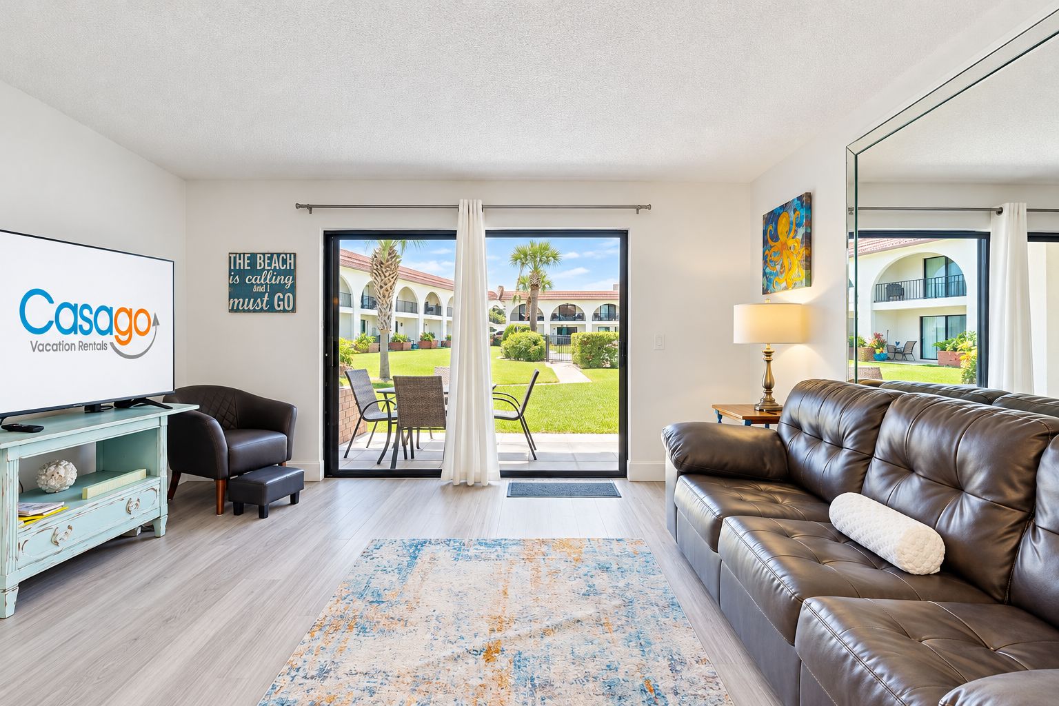 A modern living room with a television, leather sofa, and a view of a courtyard.