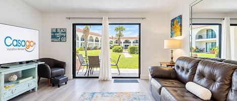 A modern living room with a television, leather sofa, and a view of a courtyard.