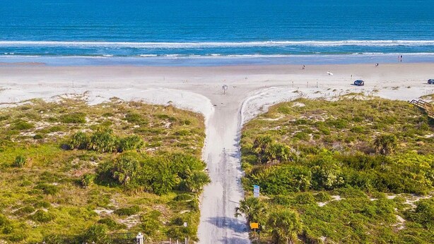 Una playa con una carretera que lleva a la orilla, rodeada de vegetación.