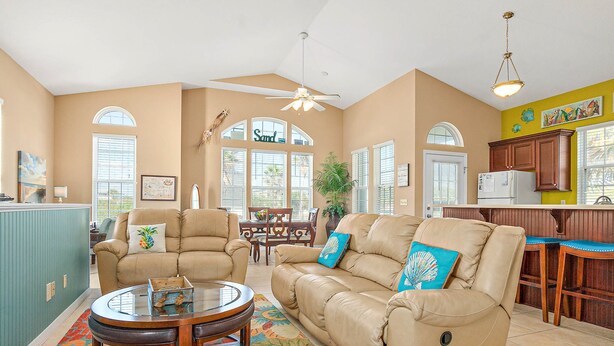 A spacious living area with a beige sofa, a round coffee table, and a dining table with chairs. - Two-level Home With Partial Ocean View, Balcony, Wifi, & W/D - Walk to the Beach (St. Augustine)