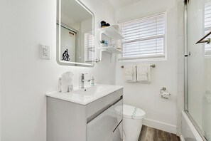 Un baño moderno con tocador blanco, un espejo grande, inodoro y zona de ducha.