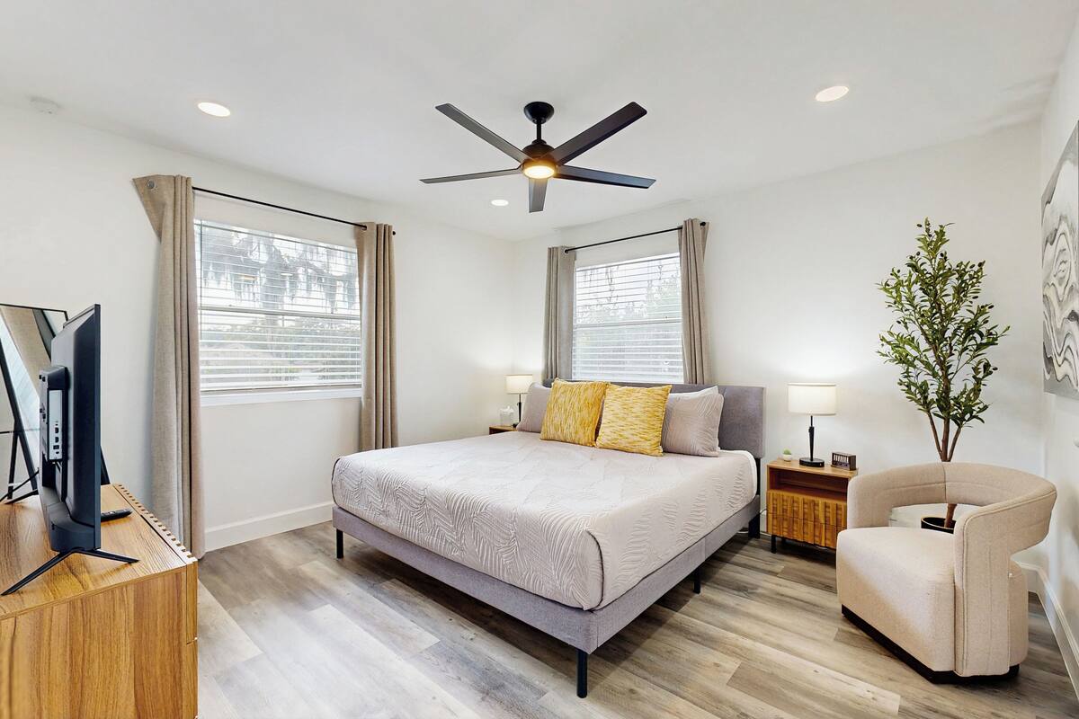 A modern hotel room with a bed, a desk, a chair, a ceiling fan, and a plant.