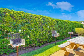 A picnic table and benches in a garden with a neatly trimmed hedge and a clear blue sky. - Third-floor Oceanfront Condo With Balcony, W/d, Pool & Tennis (Fernandina Beach)