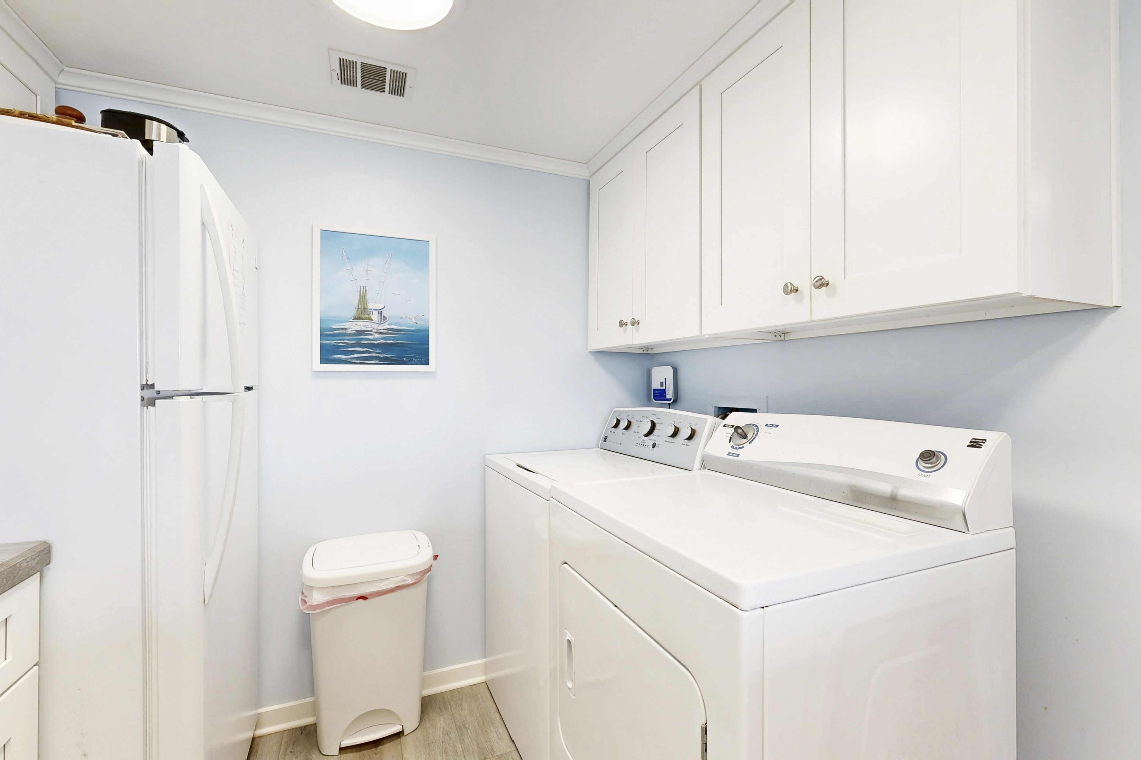 A laundry room with a washing machine, a dryer, a trash bin, and a wall-mounted heater.