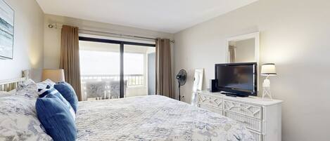 Habitació d'hotel amb un llit gran, televisió, un aparador i un balcó amb cortines.
