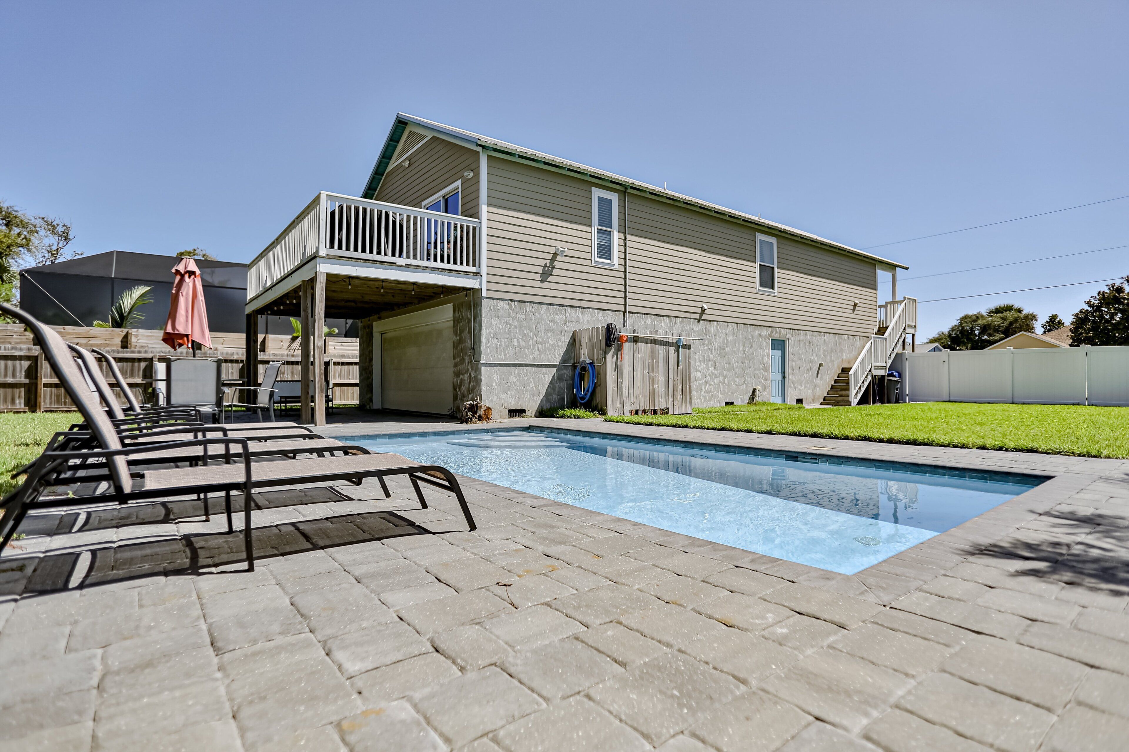 Une piscine avec des chaises longues, un patio couvert et une maison à deux étages dotée d’un balcon.