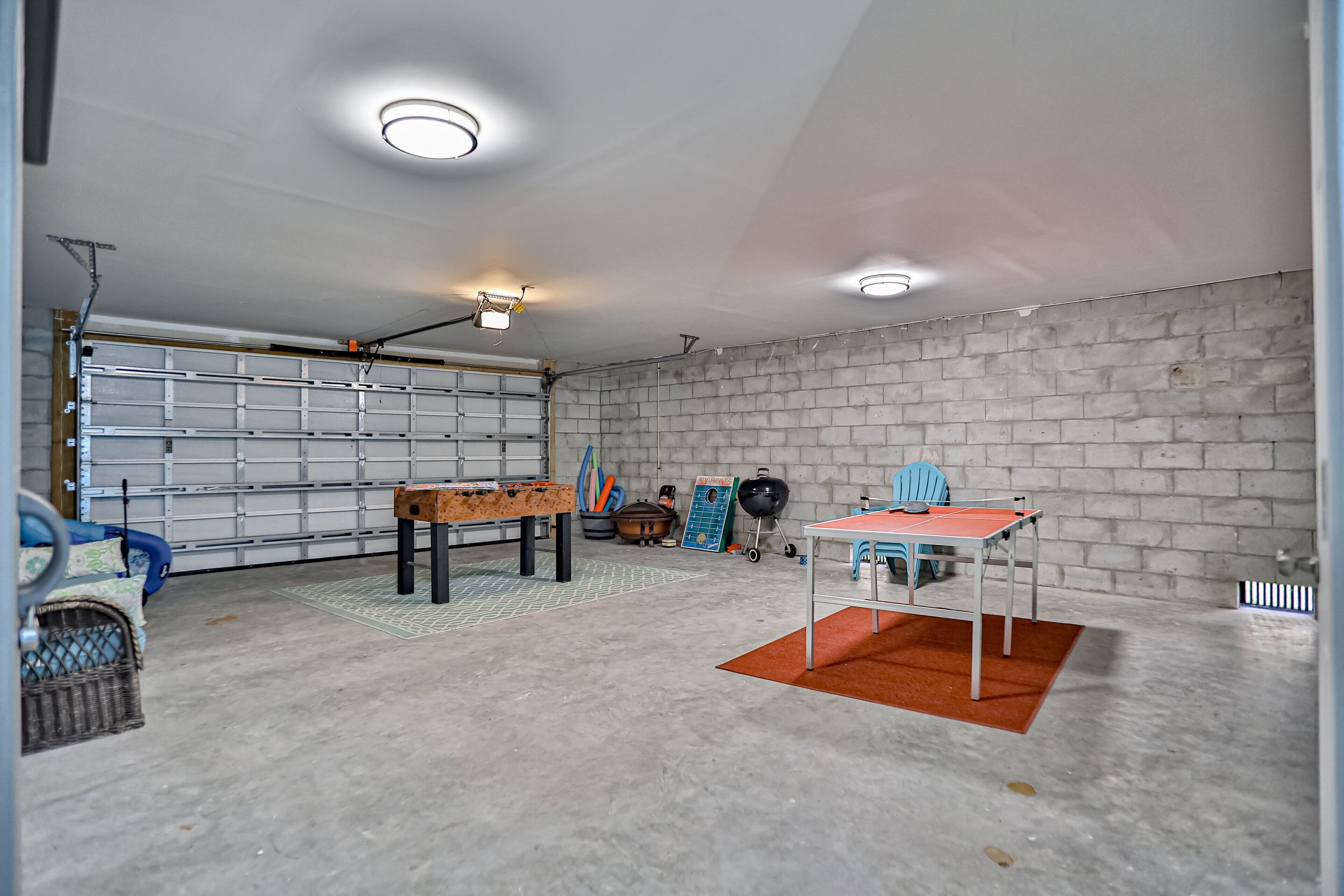 Un garaje con piso de concreto, pared de ladrillo, una mesa con sillas y una mesa de ping pong.