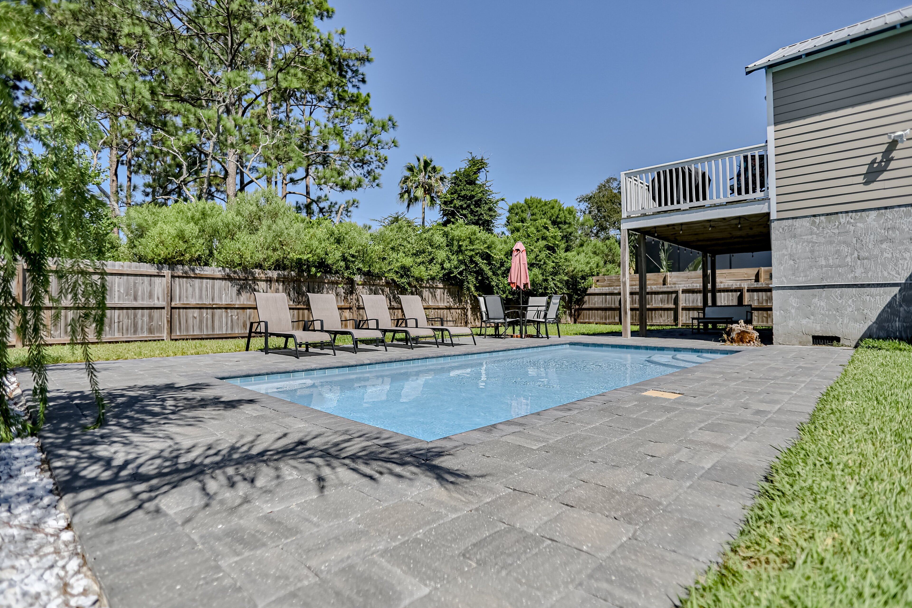 A backyard with a swimming pool, a wooden deck, and a covered patio area.