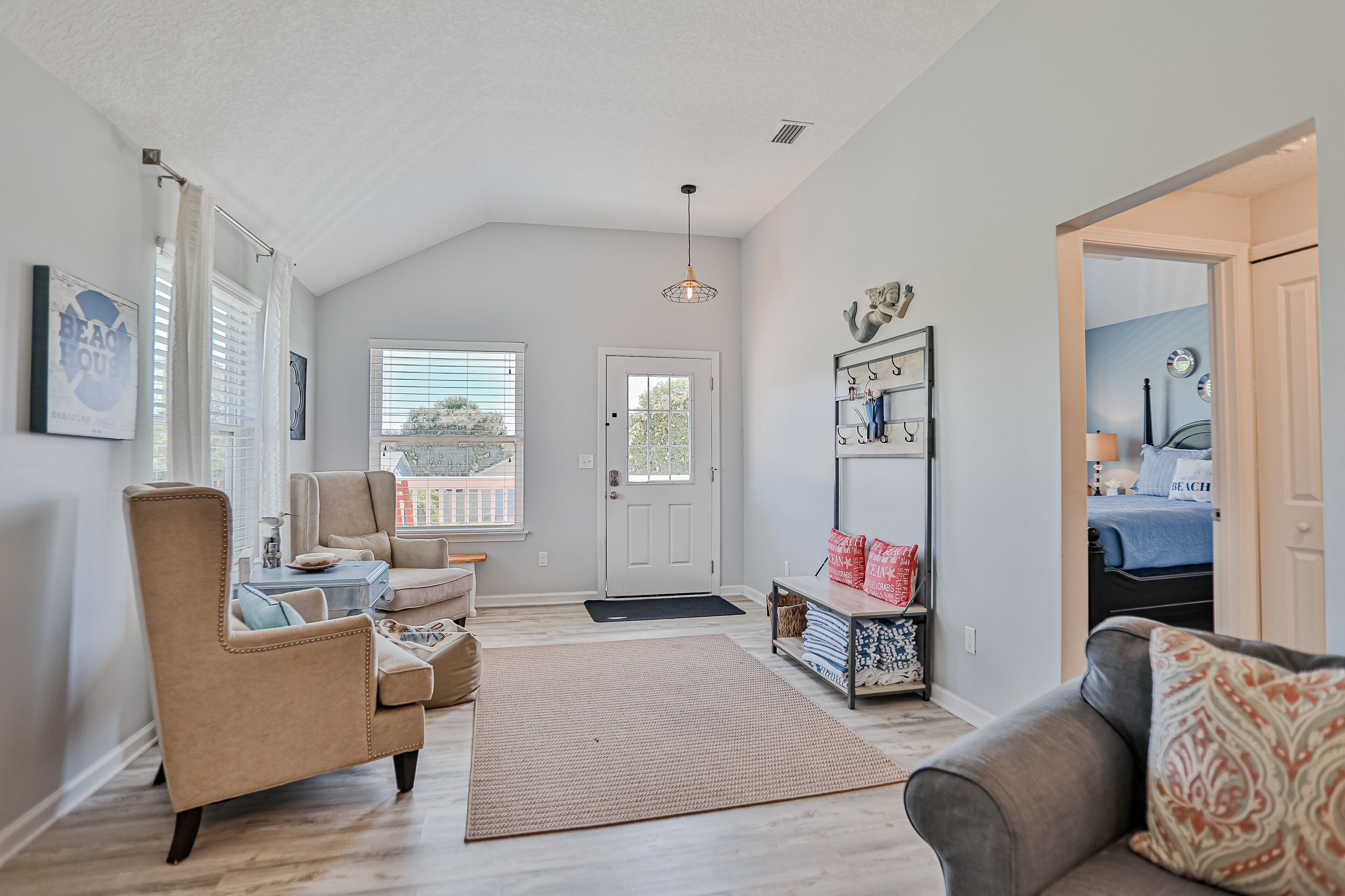 A spacious living room with a high ceiling, a large window, and a door leading to another room.