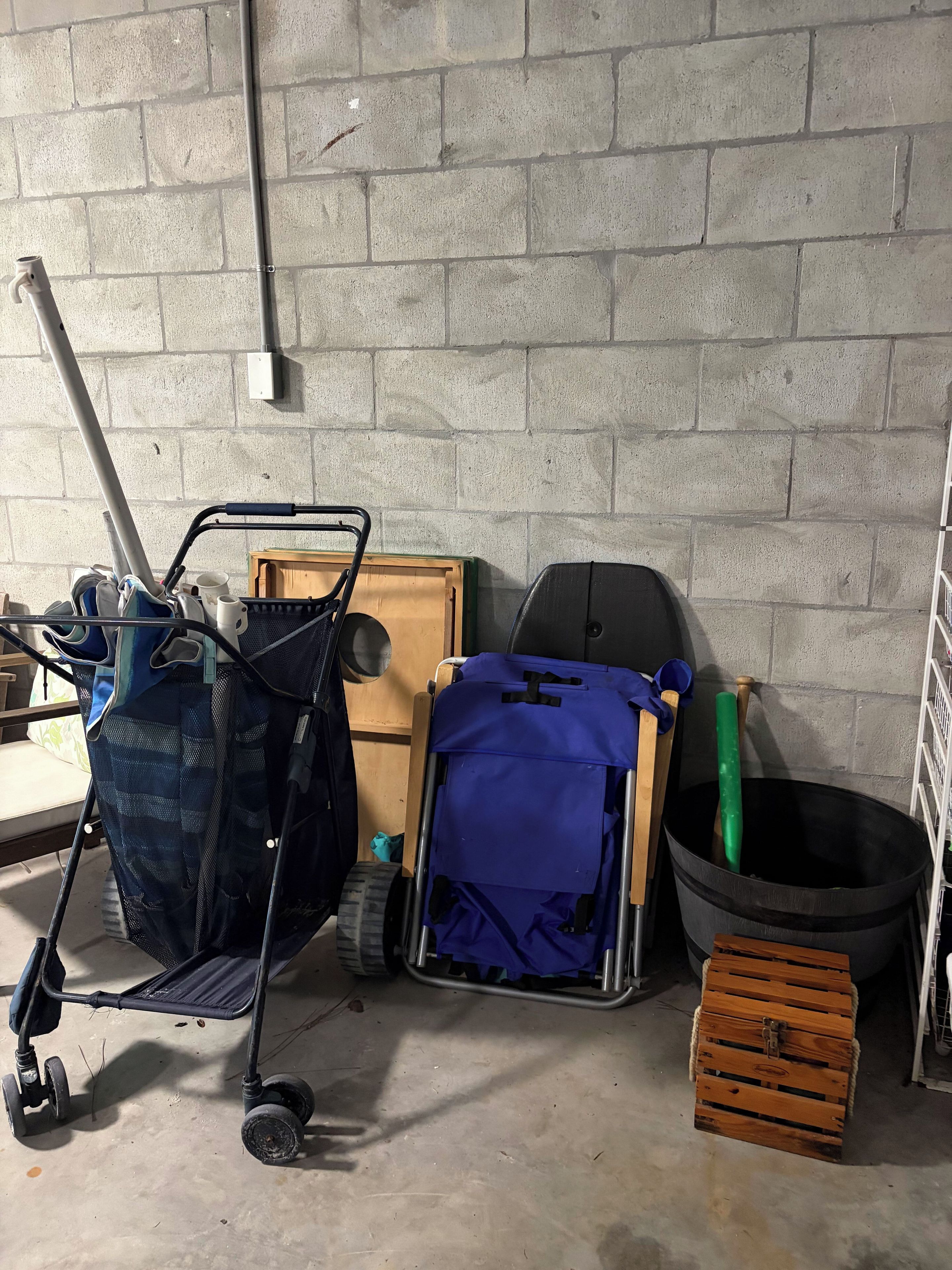 Un espacio de almacenamiento con un carrito, una maleta azul, una caja de madera y un bote negro.
