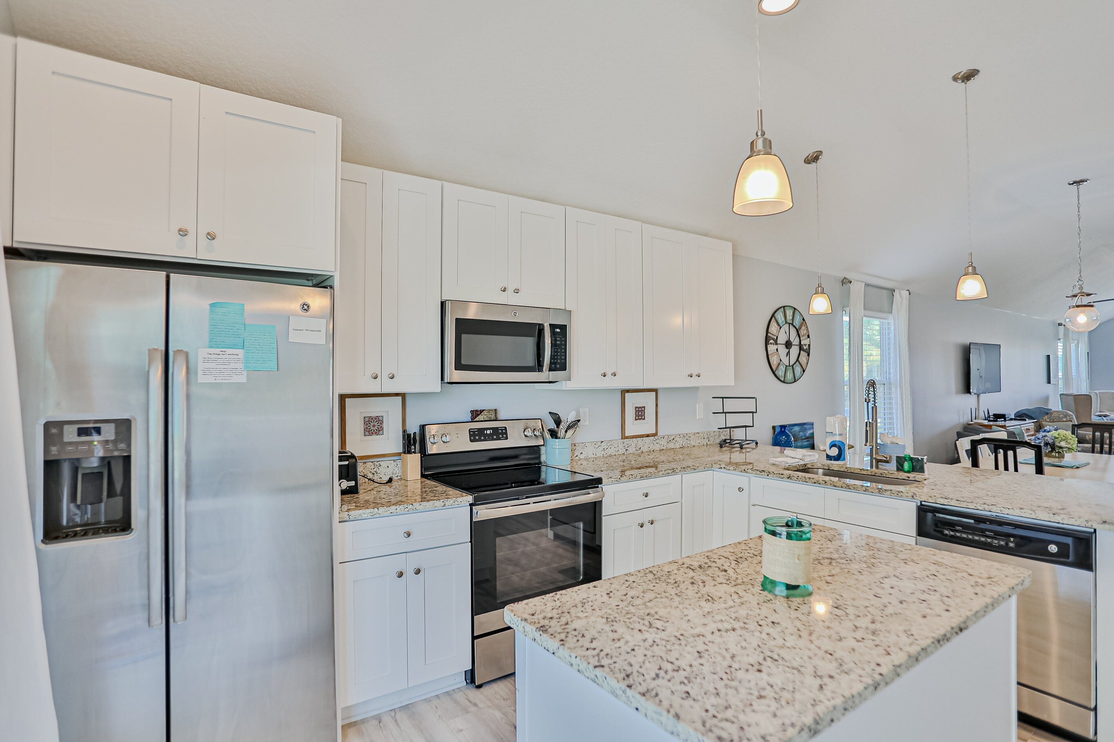 A modern kitchen with white cabinetry, stainless steel appliances, granite countertops, and pendant lighting.