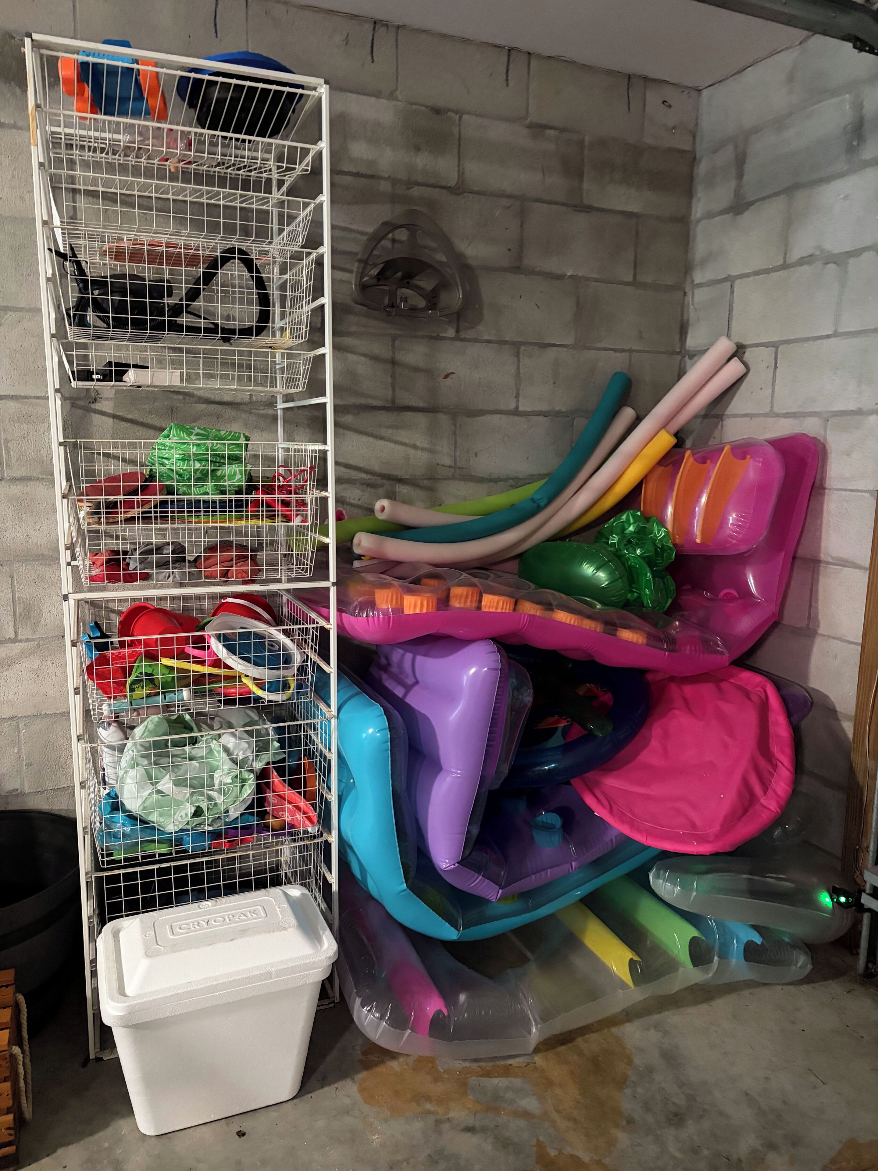 Un espace de rangement avec une étagère métallique blanche contenant divers objets, un récipient en plastique blanc et une roue fixée au mur.
