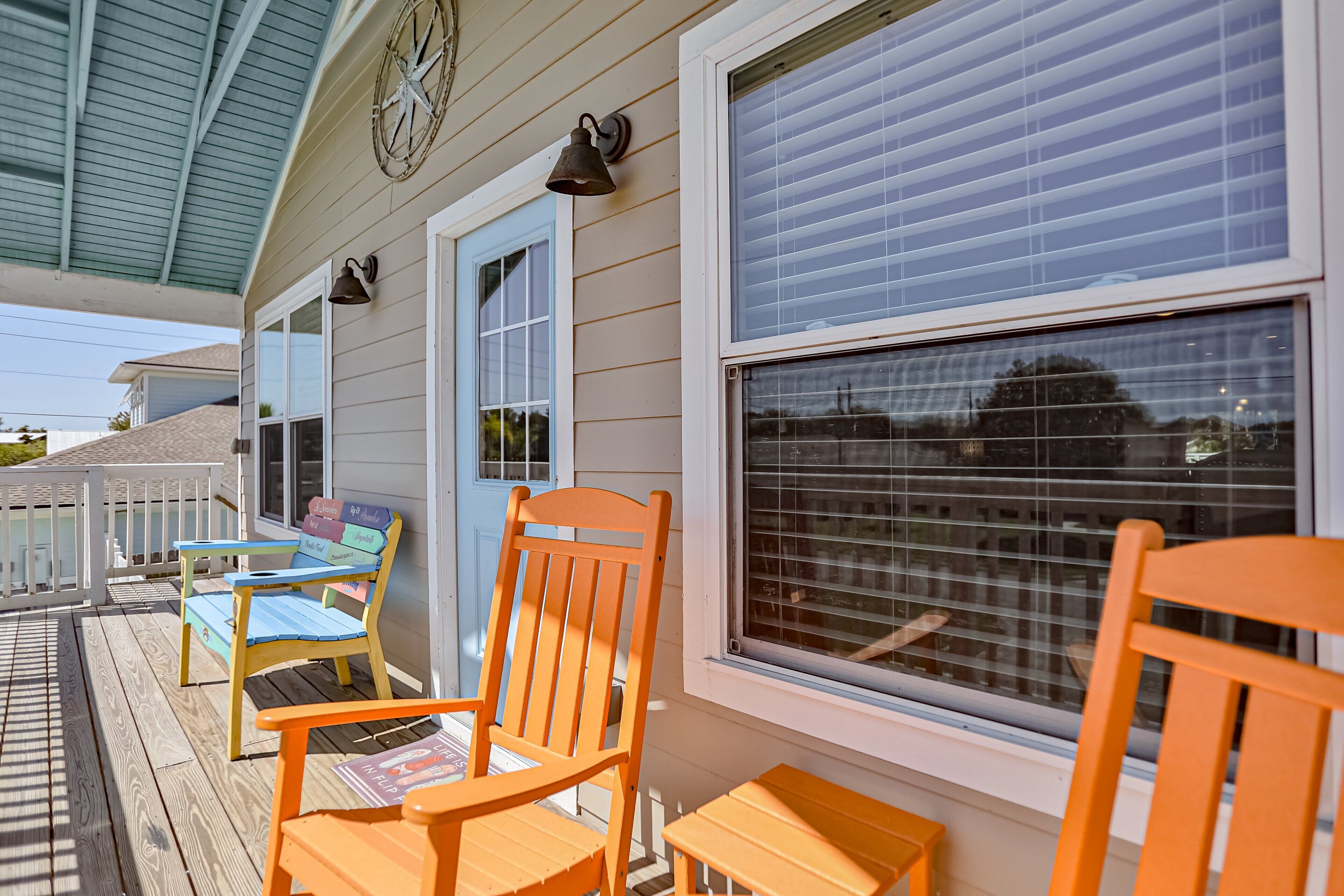 A covered porch with wooden chairs and a table, a window with blinds, and a white door.