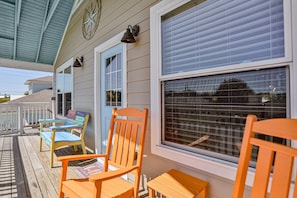 A covered porch with wooden chairs and a table, a window with blinds, and a white door. - Walk to Beach With Private Pool, Balconies & Huge Lawn Blocks to Dining (St. Augustine)