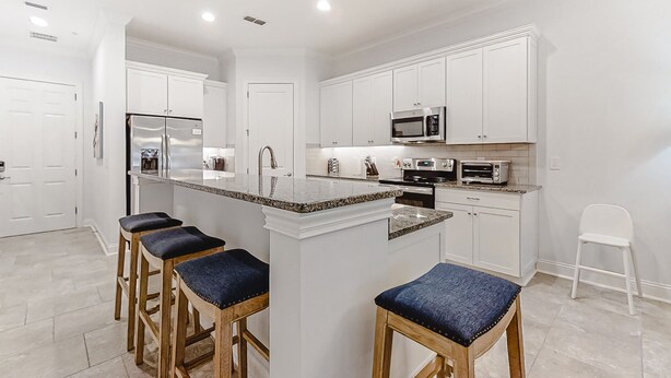 A modern kitchen with white cabinetry, a central island with bar stools, and built-in appliances. - Updated Townhome Near the Ocean W/private Patio, Shared Pool, Central A/C (Fernandina Beach)