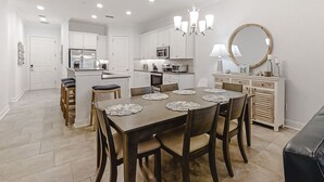 A modern kitchen with white cabinets, a dining table with placemats, and a chandelier. - Updated Townhome Near the Ocean W/private Patio, Shared Pool, Central A/C (Fernandina Beach)