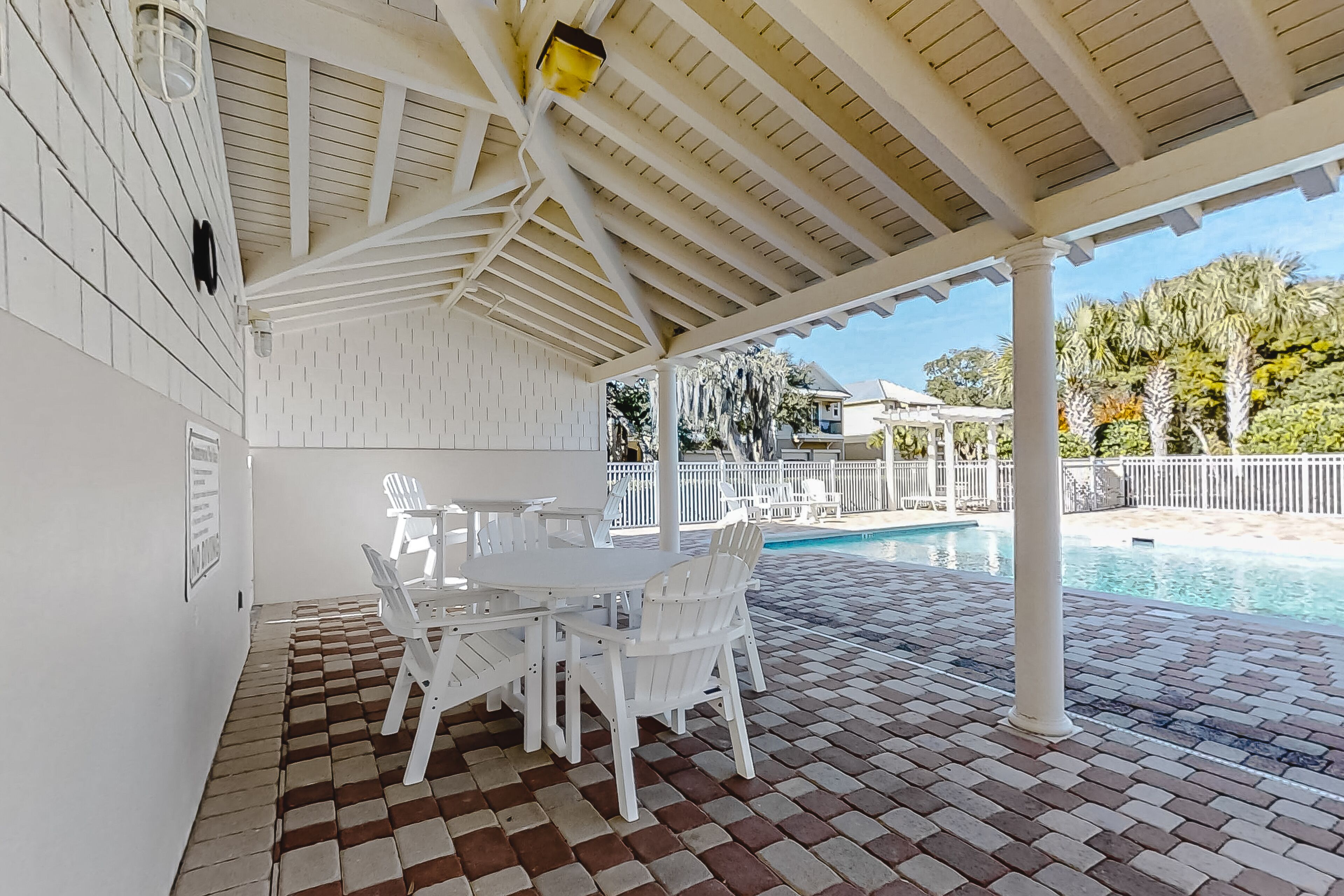 A covered patio with a pool, white furniture, and a brick floor.
