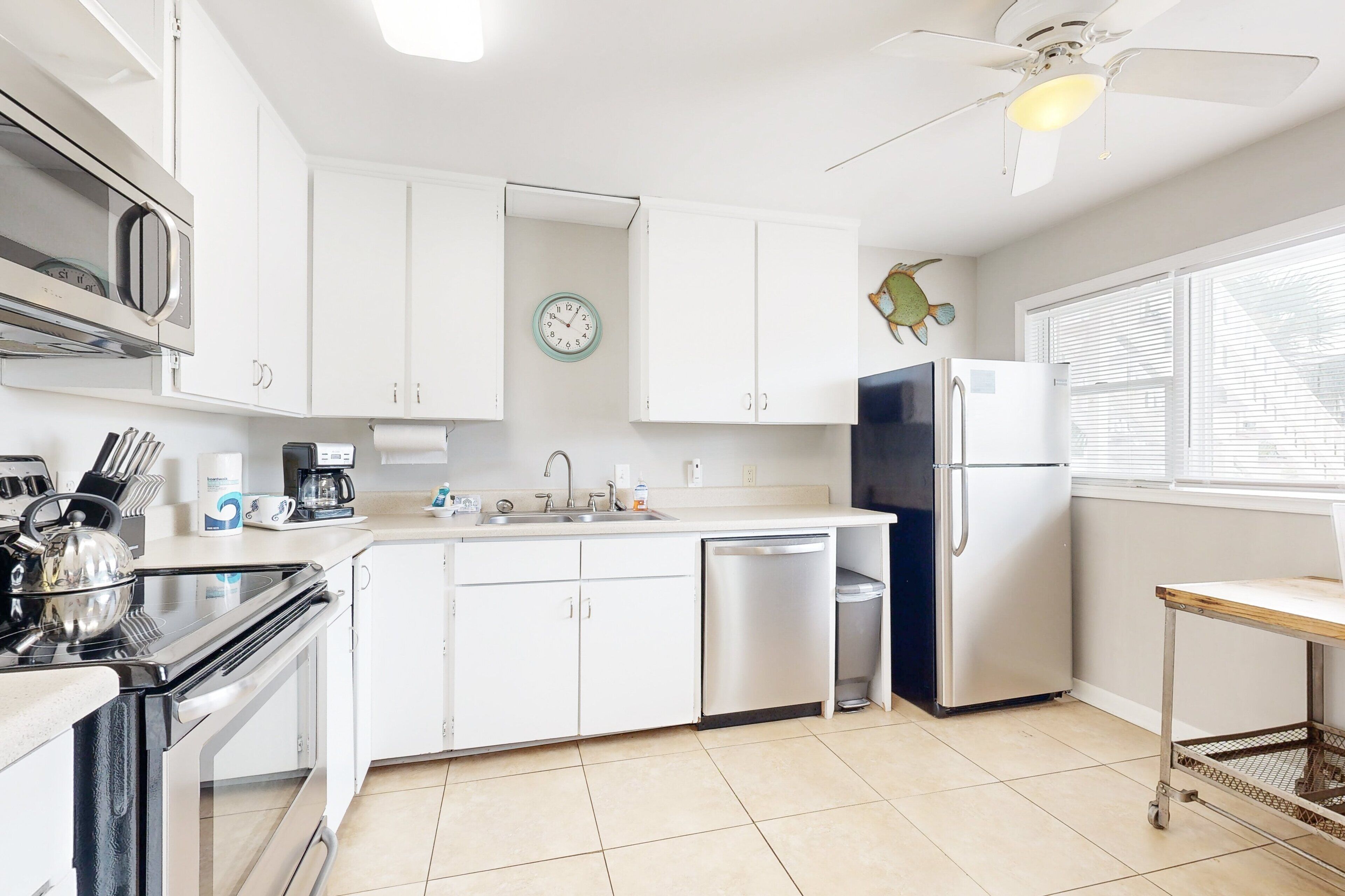 A modern kitchen with white cabinets, stainless steel appliances, a clock, and a ceiling fan.