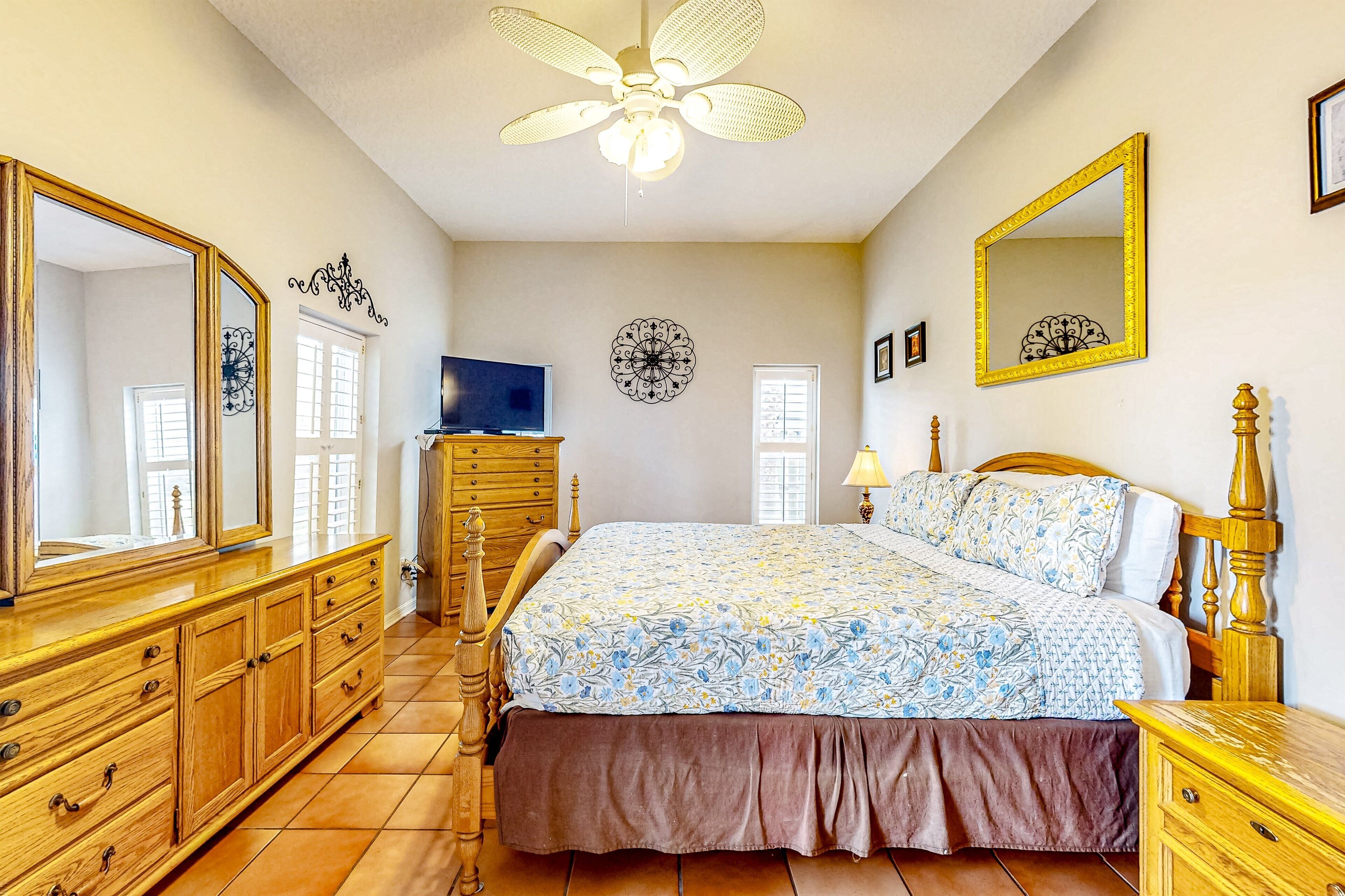 Quarto com uma cama grande, cômoda, televisão e ventilador de teto.