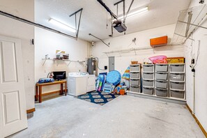A compact utility room with a washing machine, shelves with storage bins, and a projector mounted on the ceiling. - Tropical Gem w/ Courtyard & Large Deck Stroll 1 Block to Beach Boardwalk (St. Augustine)