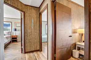 Ein Zimmer mit Holzwandverkleidung, einem Bett, einem Nachttisch, einer Lampe und einem gerahmten Bild an der Wand.
