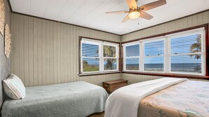 Ein Schlafzimmer mit zwei Einzelbetten, einem Deckenventilator und großen Fenstern mit Jalousien.