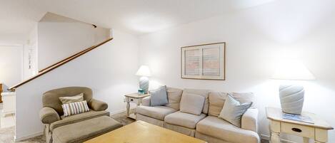 Una sala de estar con sofá, sillón, mesa de centro y lámpara.