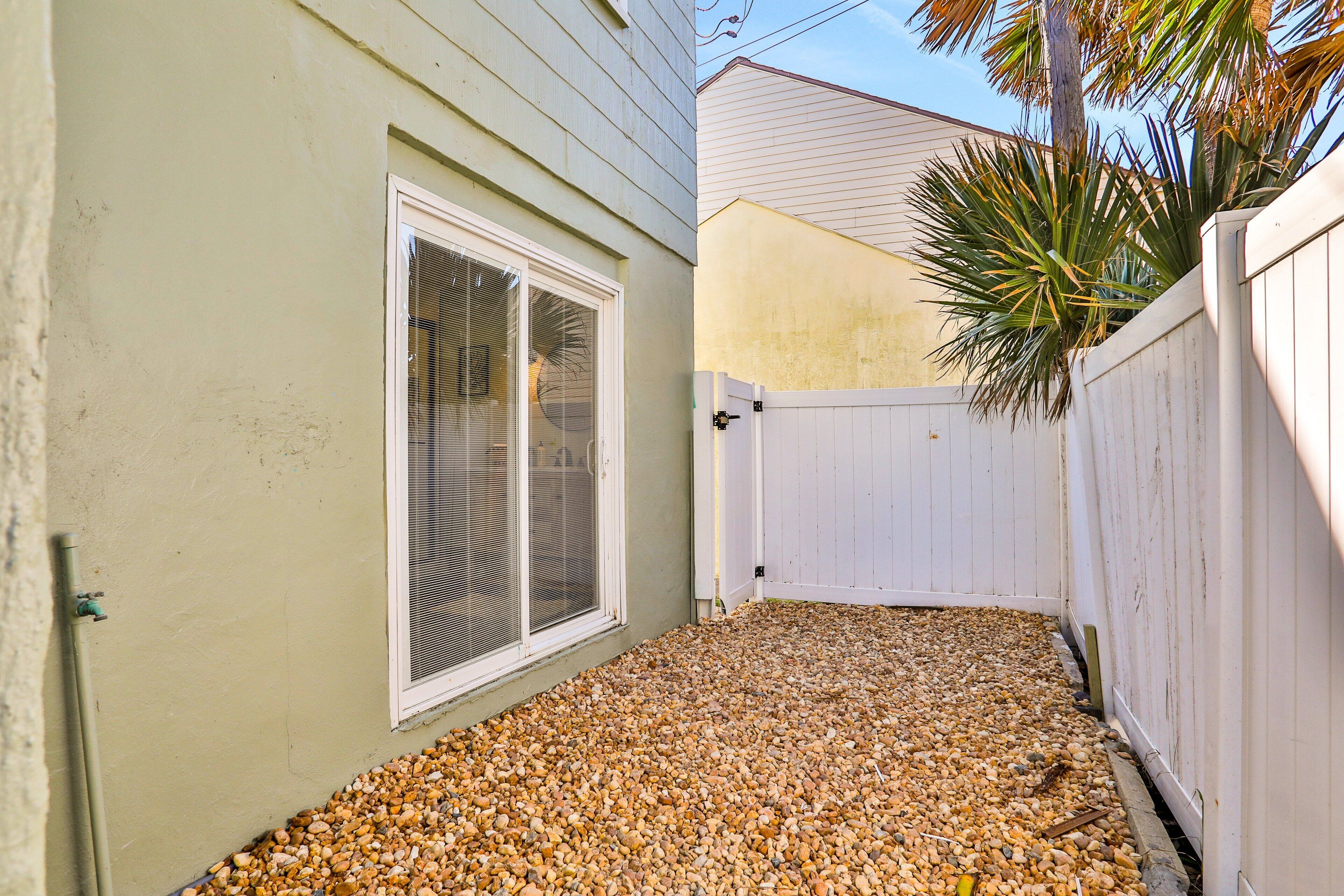 A small, enclosed backyard with a gravel ground, a white fence, and a palm tree.