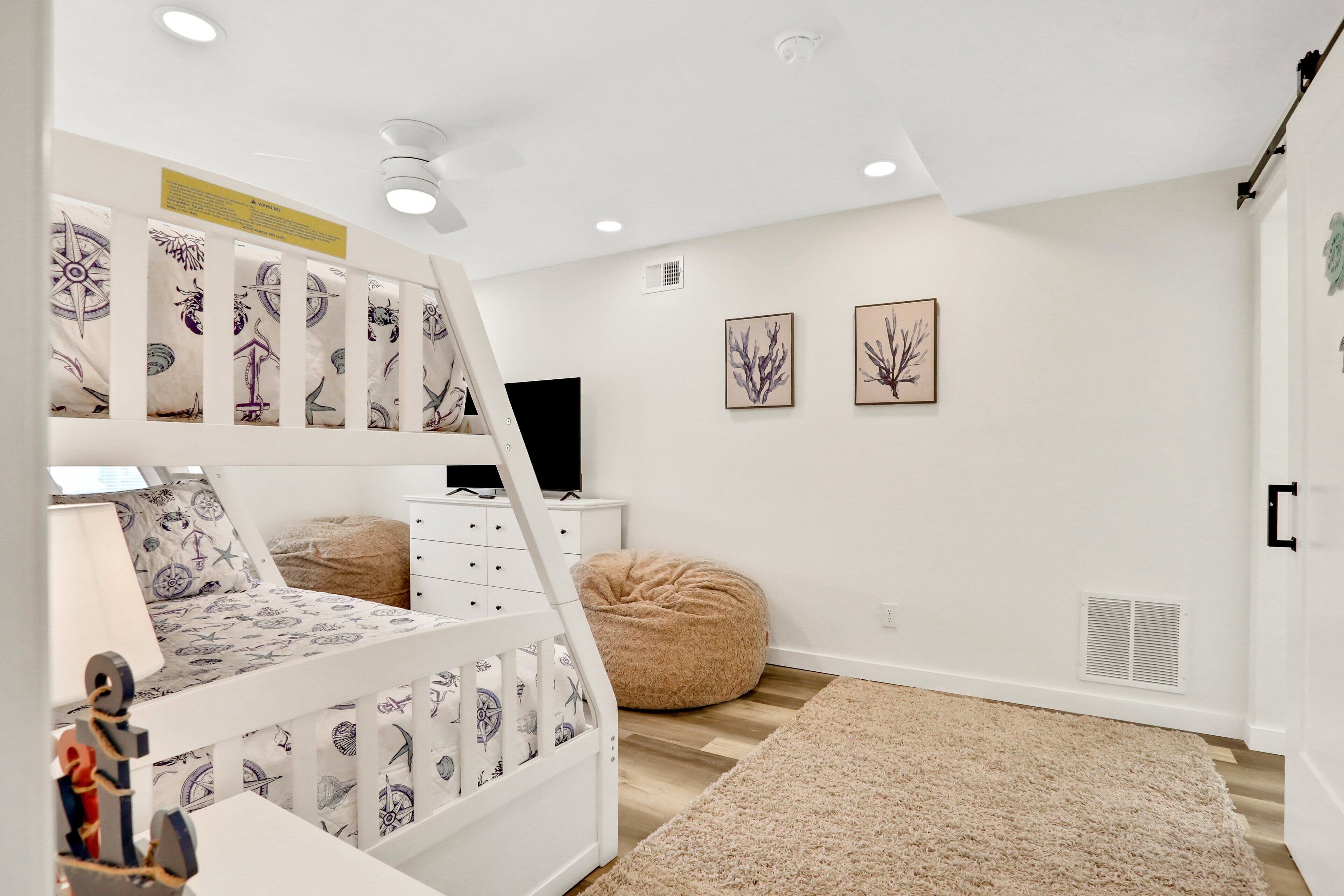 Une chambre d’enfant avec un lit superposé, un bureau, un fauteuil en forme de poire et deux tableaux encadrés accrochés au mur.