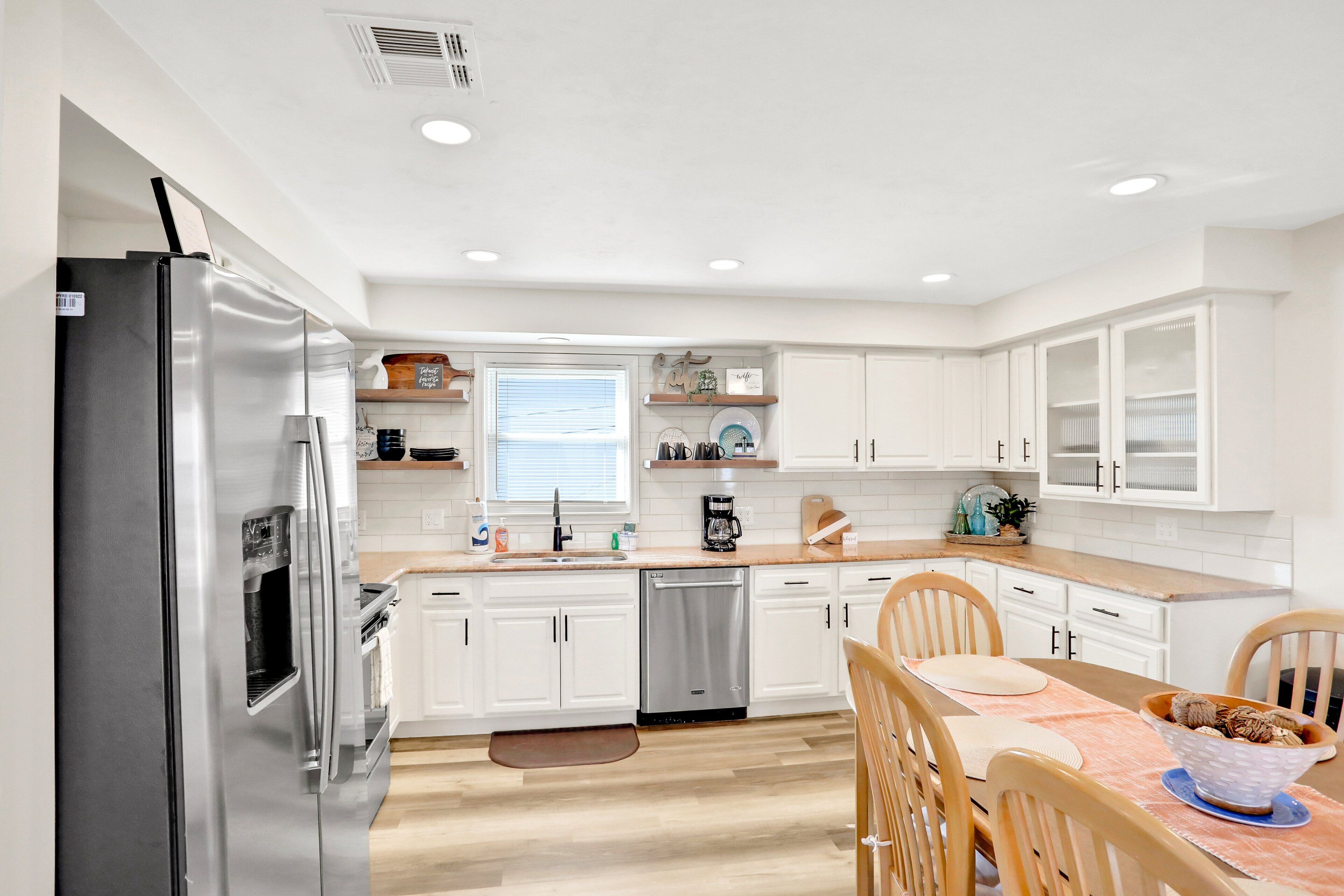 A modern kitchen with white cabinets, stainless steel appliances, and a wooden dining table.