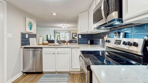 Una cocina moderna con armarios blancos, lavavajillas de acero inoxidable, estufa negra y salpicadero de azulejos azules.