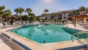 A clear swimming pool with lounge chairs and palm trees, surrounded by a building with multiple balconies. - Waterfront Condo With Community Pools & hot tub - Walk to the Beach (St. Augustine)