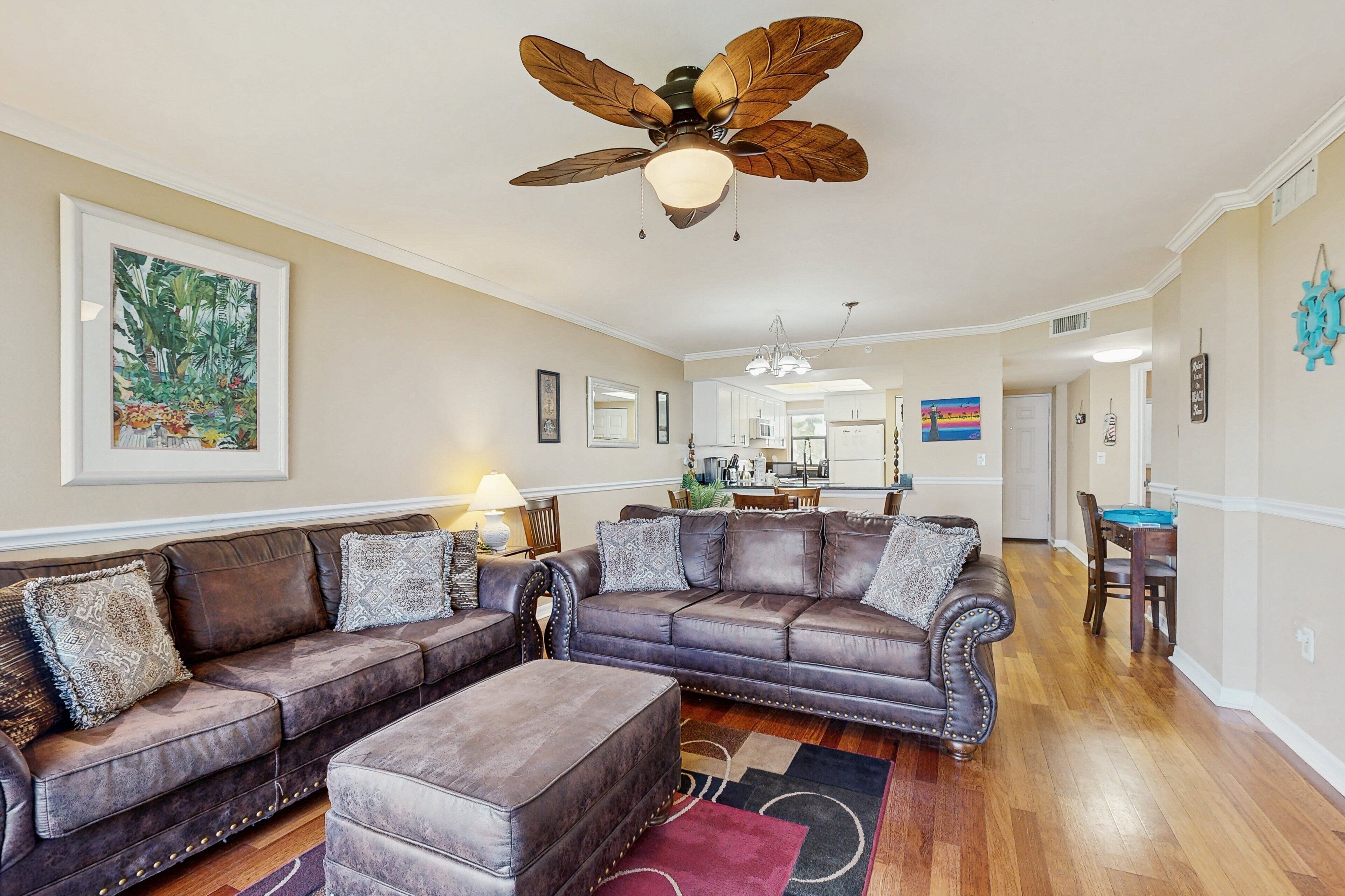 A spacious living room with a large sectional sofa, a ceiling fan, and a dining area in the background.