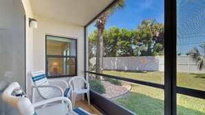 A balcony with white chairs and a table, overlooking a backyard with a palm tree and a fence. - Waterfront Condo With Community Pools & hot tub - Walk to the Beach (St. Augustine)